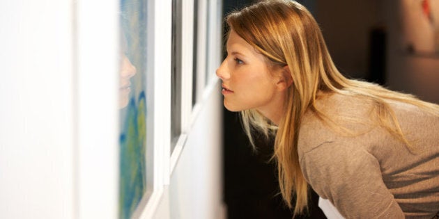 A young woman leaning over and closely examining a painting