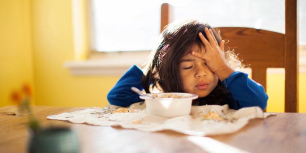 Tired toddler girl sitting at breakfast table.