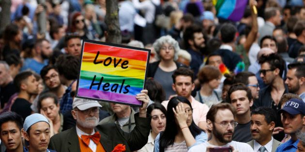 A man walks through the crowd holding a sign during a vigil and memorial for victims of the Orlando nightclub shootings near the historic Stonewall Inn, a gay bar, Monday, June 13, 2016, in New York. State and city officials, LGBT community members, and others gathered as a show of solidarity with the victims and survivors of the Orlando nightclub shootings, the worst mass shooting in modern U.S. history. (AP Photo/Kathy Willens)