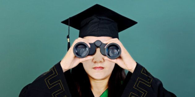 Female graduate looking through binoculars against green background.