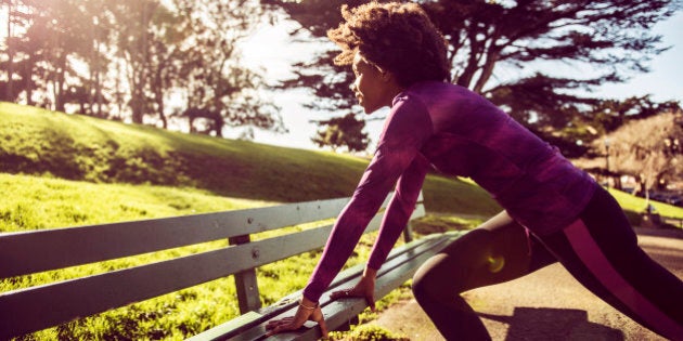 Young Woman Stretching On Park Bench