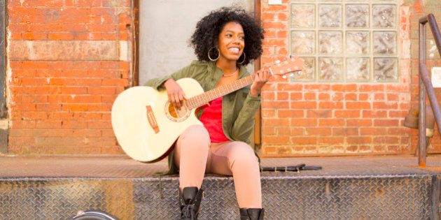 Mixed race woman playing guitar in city