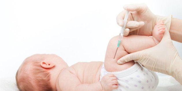 Close-up shot of pediatrician giving a three month baby girl intramuscular injection in leg on white background