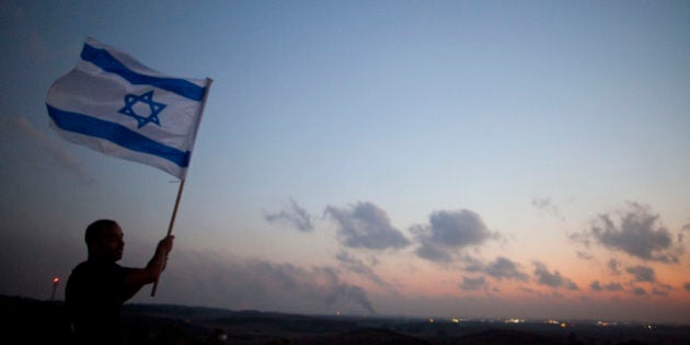 SDEROT, ISRAEL - JULY 20: (ISRAEL OUT) A man stands with an Israeli flag on a hill overlooking the Gaza Strip on July 20, 2014 near Sderot, Israel. Thirteen Israeli soldiers were killed Sunday in battle in the Gaza Strip, bringing the number of Israeli fatalities over the course of the operation to 20. At least 130 Palestinians have been killed since Israel began its ground incursion last week. (Photo by Lior Mizrahi/Getty Images)