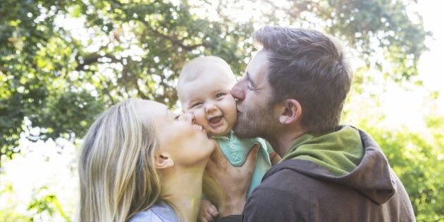 Caucasian couple kissing baby in backyard