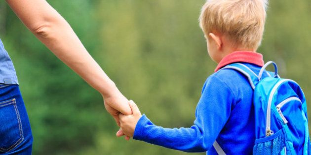 Mother holding hand of little son with backpack outdoors, back to school