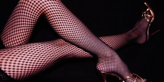 Woman legs with gold high heels and fishnet stockings on black background.