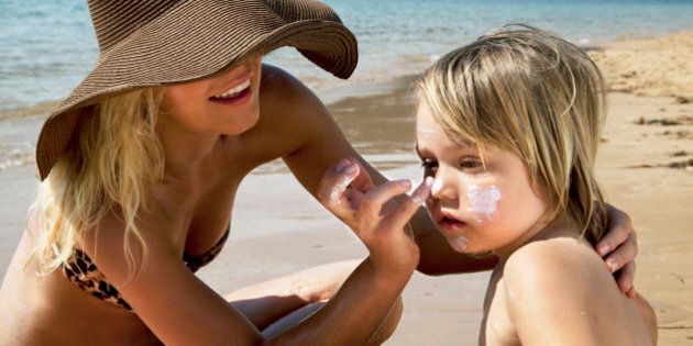 Mother putting sunscreen on her son at the beach