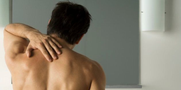 Bare-chested man touching his back, rear view
