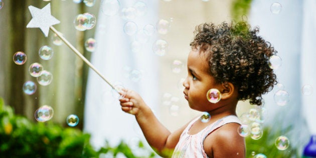 Toddler girl with star wand playing with bubbles in backyard during birthday party