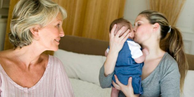 Mother kissing baby boy (2-4 months) with grandmother watching in bedroom