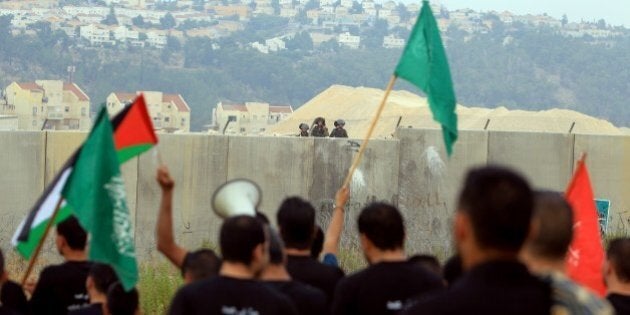 Palestinian protesters, holding national flags and the flag of the Islamist Hamas movement (green), take part in a demonstration in front of the Israeli built controversial separation barrier in the West Bank village of Bilin, on July 28, 2014, in support of Palestinians from the Gaza Strip. The protesters performed the Eid al-Fitr prayer in front of the separation barrier, protesting against the ongoing Israeli military offensive in the Palestinian enclave. The Muslim three-day Eid al-Fitr festival, that marks the end of the fasting month of Ramadan, began notably in Saudi Arabia, Egypt, Palestinian territories, Kuwait, Lebanon, Qatar, Syria or Yemen, where reports of sightings of the new moon were received. AFP PHOTO / ABBAS MOMANI (Photo credit should read ABBAS MOMANI/AFP/Getty Images)