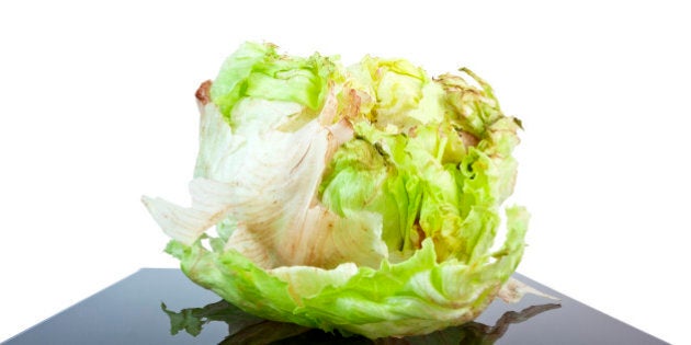 Head of iceberg lettuce beginning to spoil. Lettuce is on a black reflective stand. Reddish brown rust on leaves indicates spoilage. Horizontal.