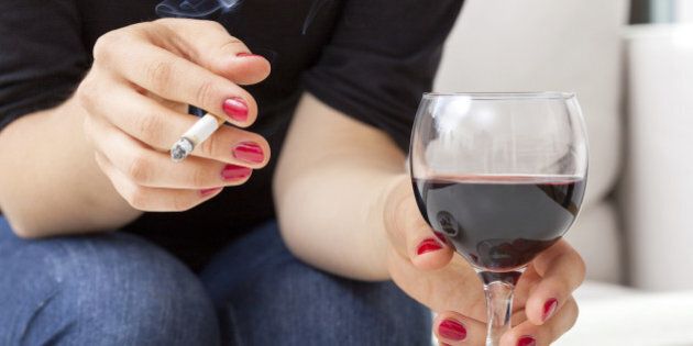 Young woman addicted to cigarettes and alcohol sitting by the table at home