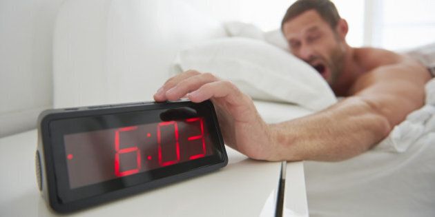 Man reaching for alarm clock from bed.