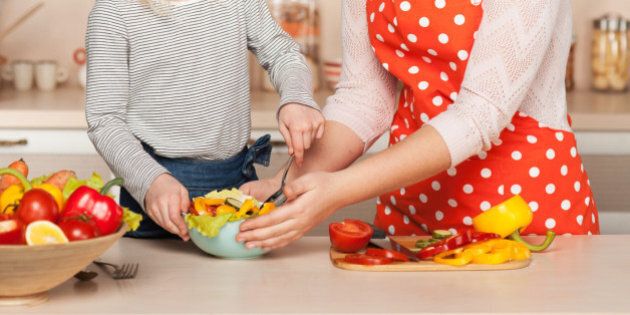 Beautiful smiling young mother and her little daughter cooking salad. Kitchen interior. Concept for young kitchen hands