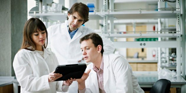 Three scientists in research laboratory discussing project on digital tablet