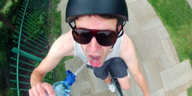 Action shot of adult man drinking water on bicycle. He is wearing a helmet and sunglasses.