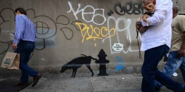 People walk by a street art graffiti by elusive British artist Banksy, as part of his month-long Better Out Than In exhibit, in New York, October 3, 2013. Banksy will be attempting to host an entire show on the streets of New York during a month residency. AFP PHOTO/Emmanuel Dunand (Photo credit should read EMMANUEL DUNAND/AFP/Getty Images)