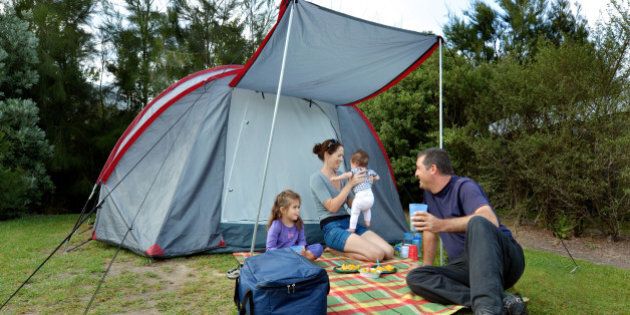 Young family, father and mother with two children camping in a tent outdoors.