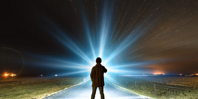 Young man shining a powerful torch on a starry night in Iceland, looking for the northern lights or aliens