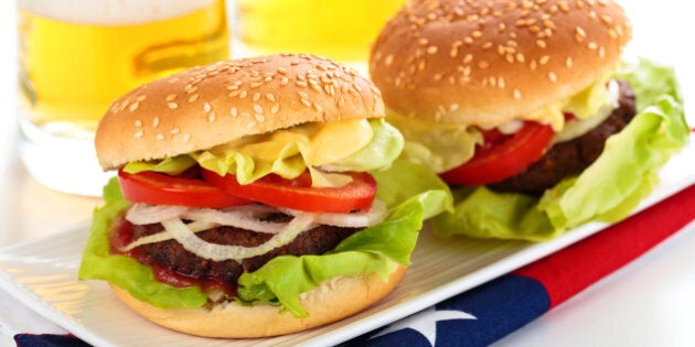 Beer and two tasty hamburgers on white table.