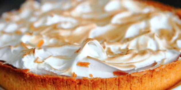 Horizontal composition color photography of close-up in selective focus part of beautiful homemade cooked lemon meringue pie, tart with pastry dough in white plate placed on a dark black grey abstract background defocused texture workplan from kitchen island, taken with large copy space background ready for design. Lemon meringue pie is a type of baked pie, usually served for dessert, made with a crust usually made of shortcrust pastry, lemon custard filling and a fluffy meringue topping. Lemon meringue pie is prepared with a bottom pie crust, with the meringue directly on top of the lemon filling. The cream is a mixture of eggs, sugar, lemon juice and lemon zest. Lemon flavored custards, puddings and pies have been enjoyed since Medieval times, but meringue was perfected in the 17th century. Lemon meringue pie, as it is known today, is a 19th-century product. The earliest recorded recipe was attributed to Alexander Frehse, a Swiss baker from Romandie. The lemon custard is usually prepared with egg yolks, lemon zest and juice, sugar, and, optionally, starch. The meringue, which includes well beaten egg whites and sugar, is cooked on top of the pie filling. As the meringue bakes, air bubbles trapped inside the protein of the egg whites will expand and swell.