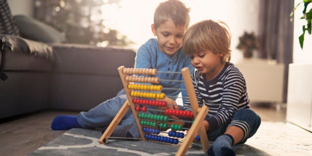 Little boy is helping his little brother to learn counting on abacus. Sunny day.