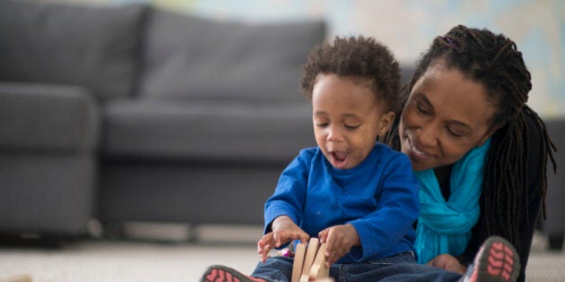 A mother is playing with her little boy in their home on mother's day. The toddler is playing with wooden building blocks.