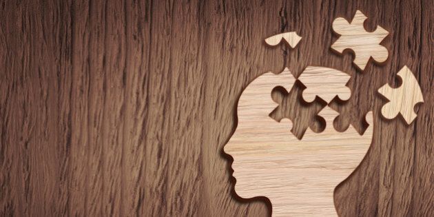 Human head silhouette with a jigsaw piece cut out on the wooden background, mental health symbol