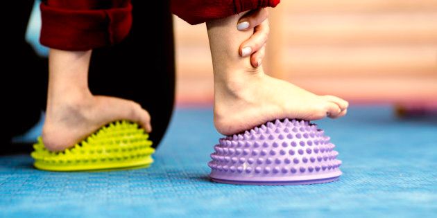 Flat Feet Corrective Exercises - Little boy walking over spikey half balance rubber balls on a physical therapy exercise class. Physical therapist helping