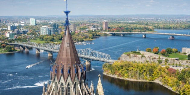 The spire of the Parliamentary Library is in the foreground and the Interprovincial and McDonald-Cartier bridges are in the background, joining Ontario and Quebec across the Ottawa River in downtown Ottawa and Gatineau.