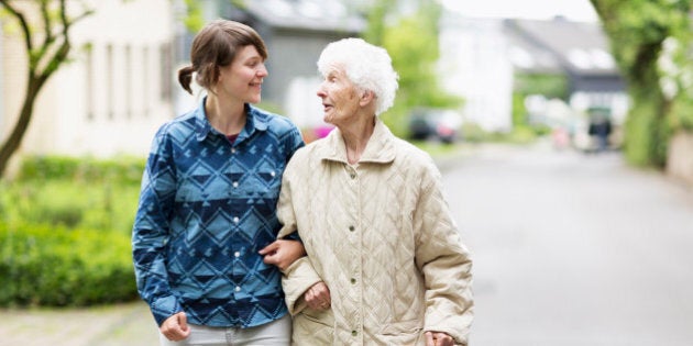 senior woman, 91 years old walking in the street supported by a crutch and a young caregiver