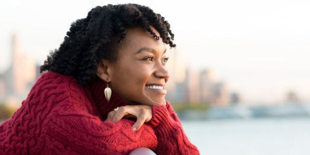 Close up portrait of a young happy african woman leaning on the banister of a bridge near river. Happy young african woman at river side thinking about the future. Smiling pensive girl looking across river at sunset.
