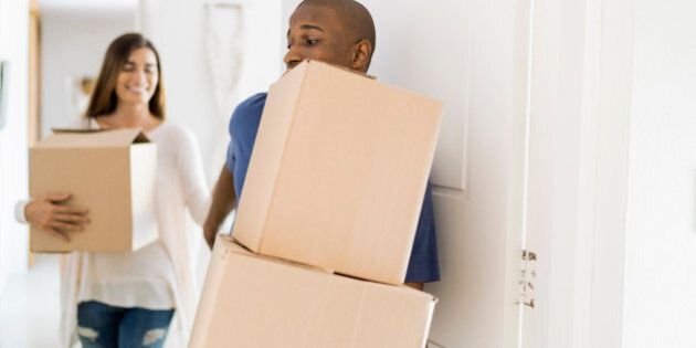 Young man and woman with cardboard boxes at doorway. Multi-ethnic couple are moving into new apartment. They are wearing casuals.