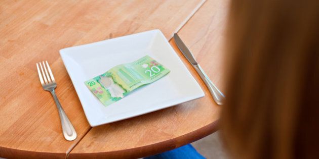 A woman sits at a table with a plate with no food but a $20 Canadian bill