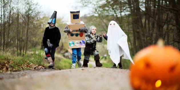Children (4-12) wearing fancy dress costumes on country lane, carved pumpkin in foreground