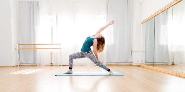 Young woman doing high lunge yoga asana in light spacious studio, virabhadrasana