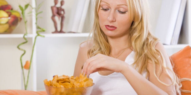 sad woman eating snacks at home while sitting on sofa