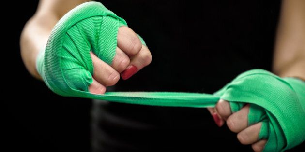 Woman is wrapping hands with green boxing wraps. Isolated on black with red nails. Strong hand and fist, ready for fight and active exercise. Women self defense.