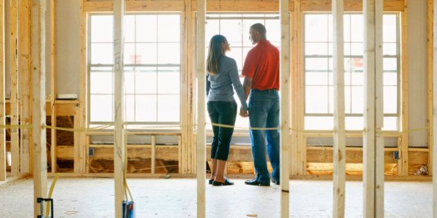 Couple holding hands in home under construction, rear view