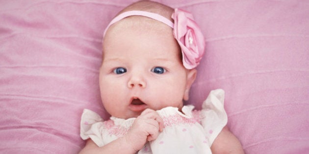 Cute beautiful newborn baby girl on a pink blanket inbeautiful tiny dress and a pink flower hairband looking at camera interested