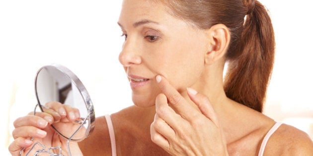 Elderly woman looking for wrinkles around the corner of her mouth in mirror