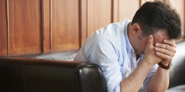 Shot of a grief-stricken man sitting on a sofa with his head in his hands