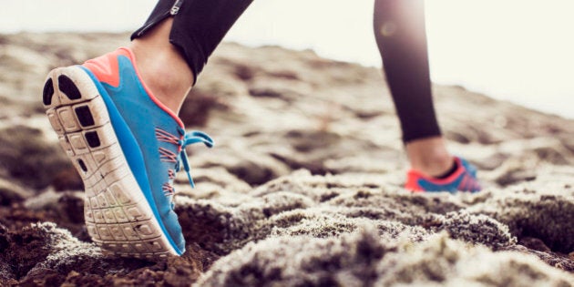 Close up, low angle shot of a female runners trainers, running through mossy terrain in Iceland. Blue trainers, black running leggings with backlit sunshine.