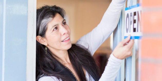 Hispanic small business owner hanging open sign on door