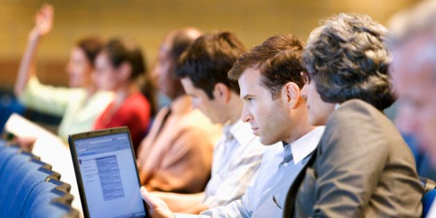 Business people sitting in lecture hall with laptop
