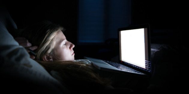 A tired young woman studying late into the night, lying almost flat as she studies her computer, the blue moon coming through two windows behind her.