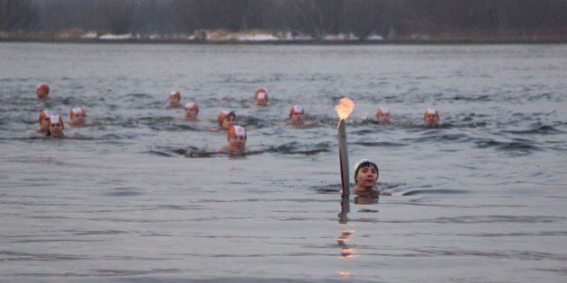 In this photo provided by Olympictorch2014.com torch bearer Natalia Usacheva, ice cold water swimmer, swims with the Olympic torch during the Olympic torch relay along the Tatyshev Channel of the Yenisei River in Krasnoyarsk, Russia, Tuesday, Nov. 26, 2013. The 65,000-kilometer (39,000 mile) Sochi torch relay, which started on Oct. 7, is the longest in Olympic history. The torch has traveled to the North Pole on a Russian nuclear-powered icebreaker and has even been flown into space. (AP Photo/Olympictorch2014.com)