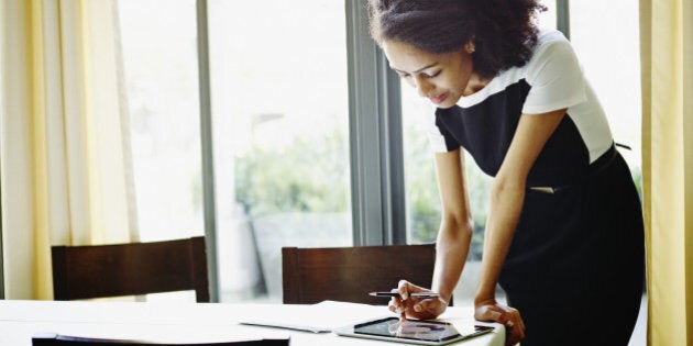 Businesswoman standing at table in restaurant looking at document on digital tablet taking notes